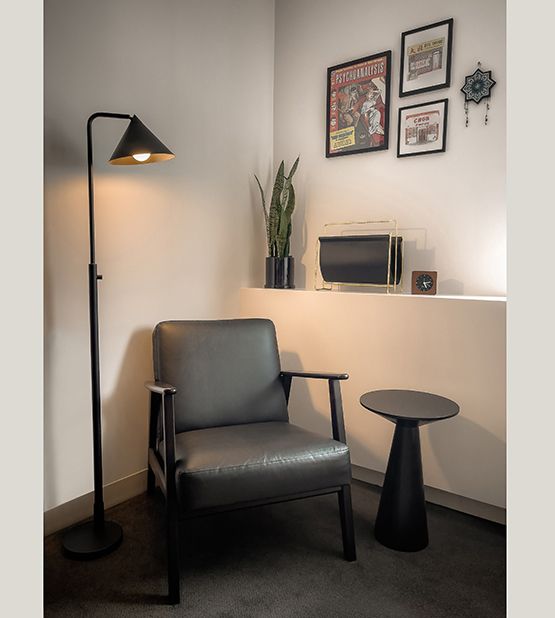 Black leather armchair with wooden frame, adjustable floor lamp, small side table, and framed posters on the wall